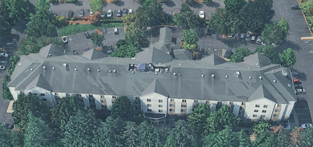 Angled aerial of the property from the side showing massing and tree perimeter